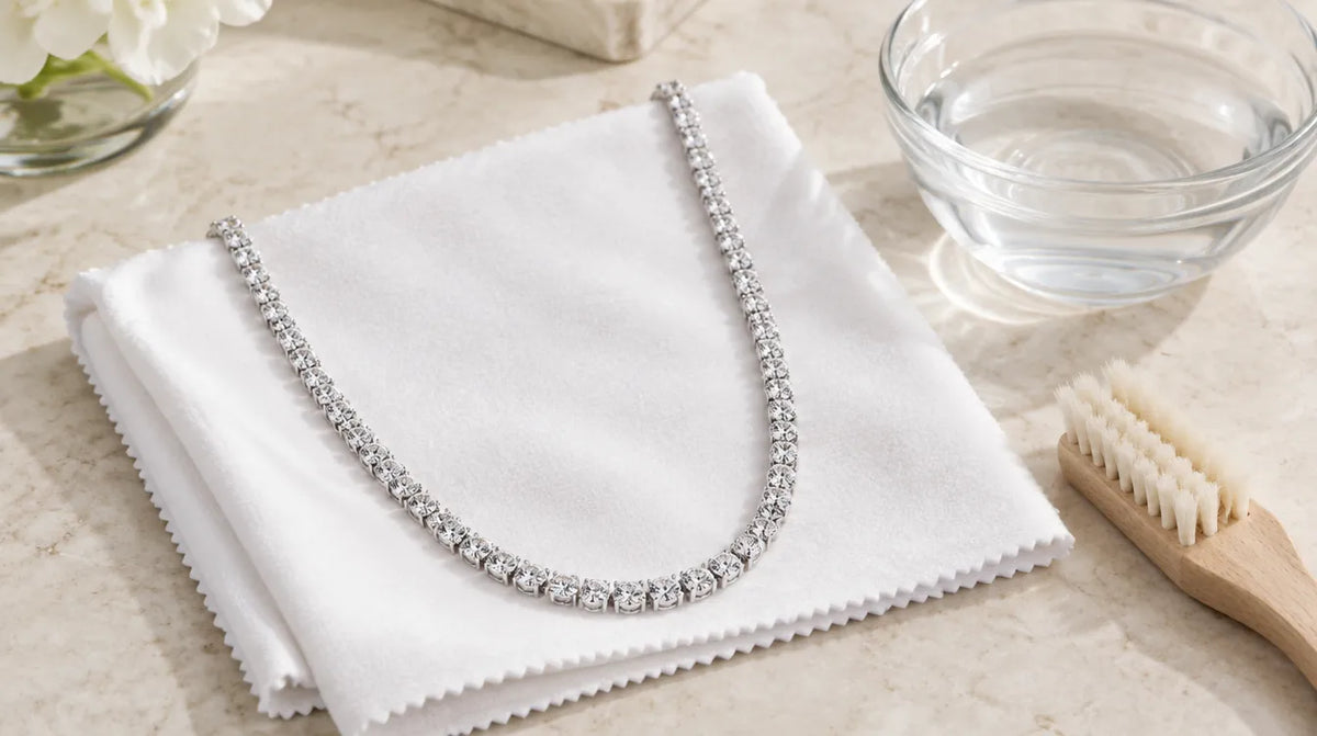 Silver tennis necklace on a polishing cloth with a bowl of water and a soft brush