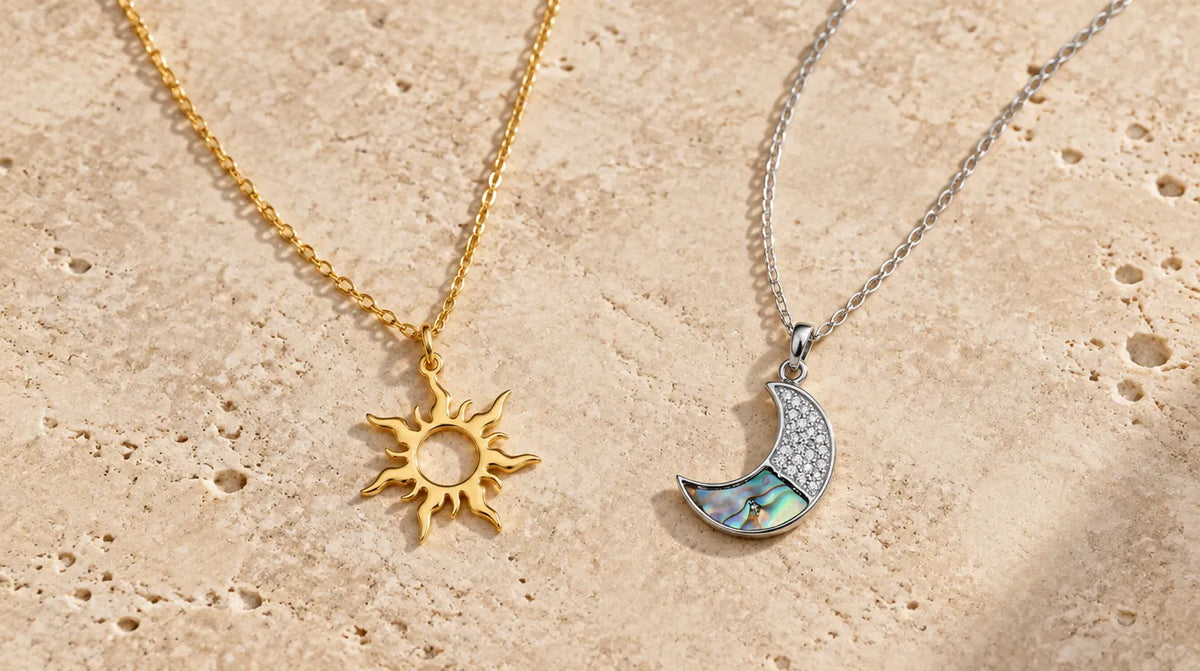 Gold-plated sun pendant and silver moon pendant side by side on travertine
